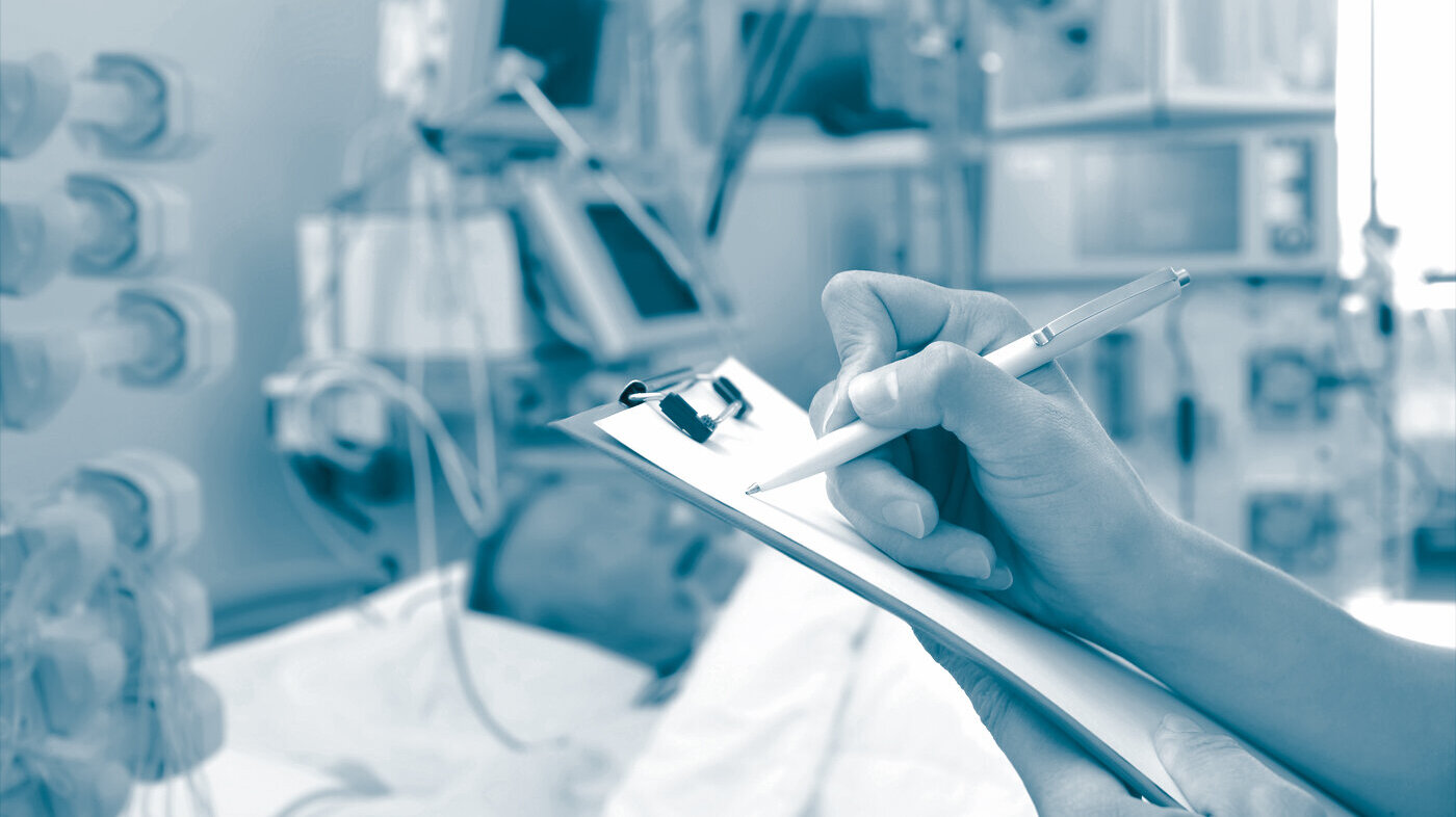 Documentation in the ICU The photo shows an ill patient in an ICU. In the foreground a nurse's hands are holding a form while writing on the form