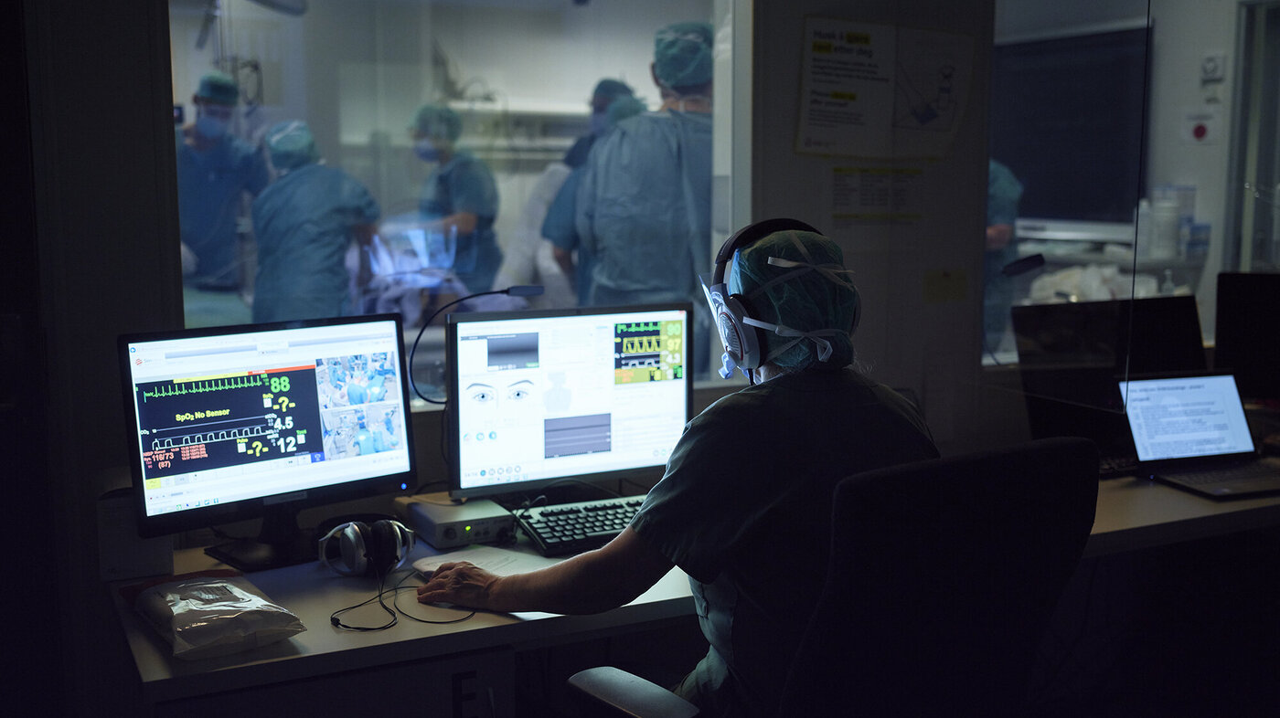 Simulering av et akutt keisersnitt Bildet viser en operatør av en simulering, som sitter og styrer det hele via tre dataskjermer, foran et ensidig speil. På andre siden foregår simuleringen