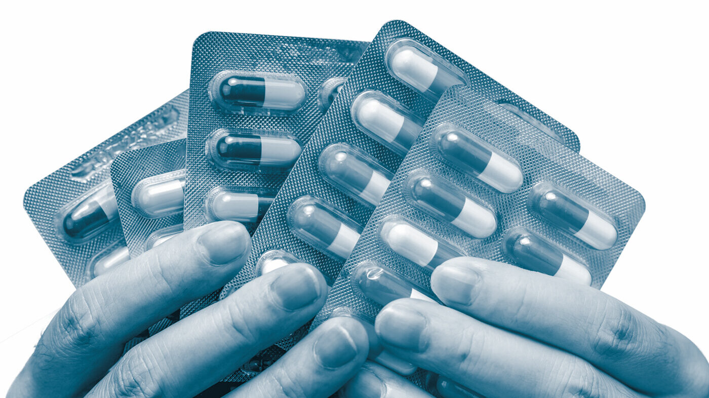 The photo shows hands holding various pills and tablets