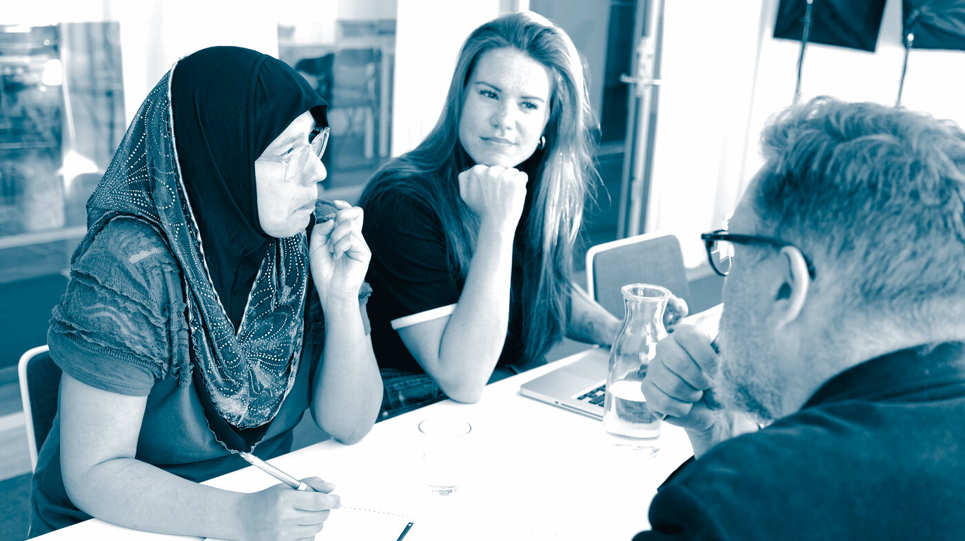 Meeting The photo shows a woman wearing a hijab, a woman wearing Western clothes and a man in a suit, sitting around a table. They are attending a meeting.