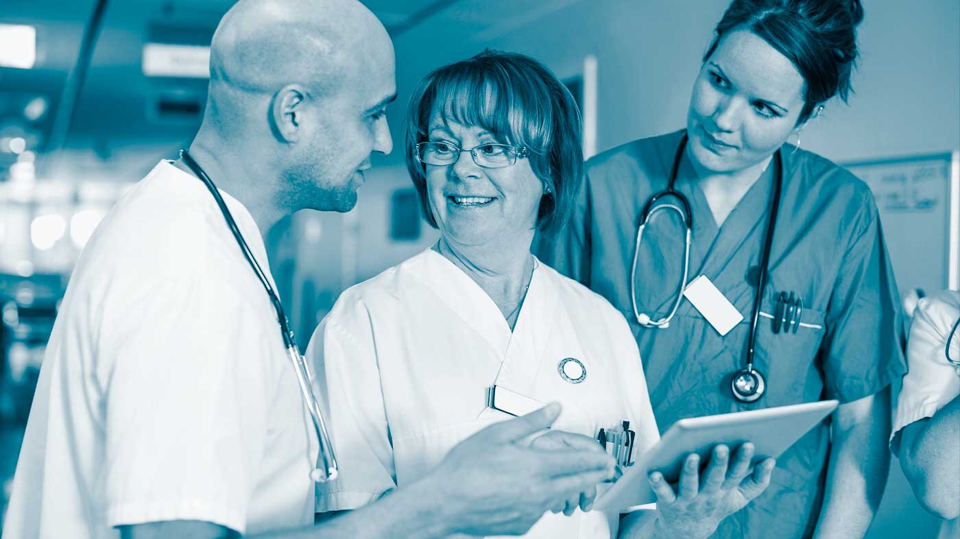 The photo shows three health professionals:  a man and two women. The woman in the middle is holding a form. They are smiling at each other