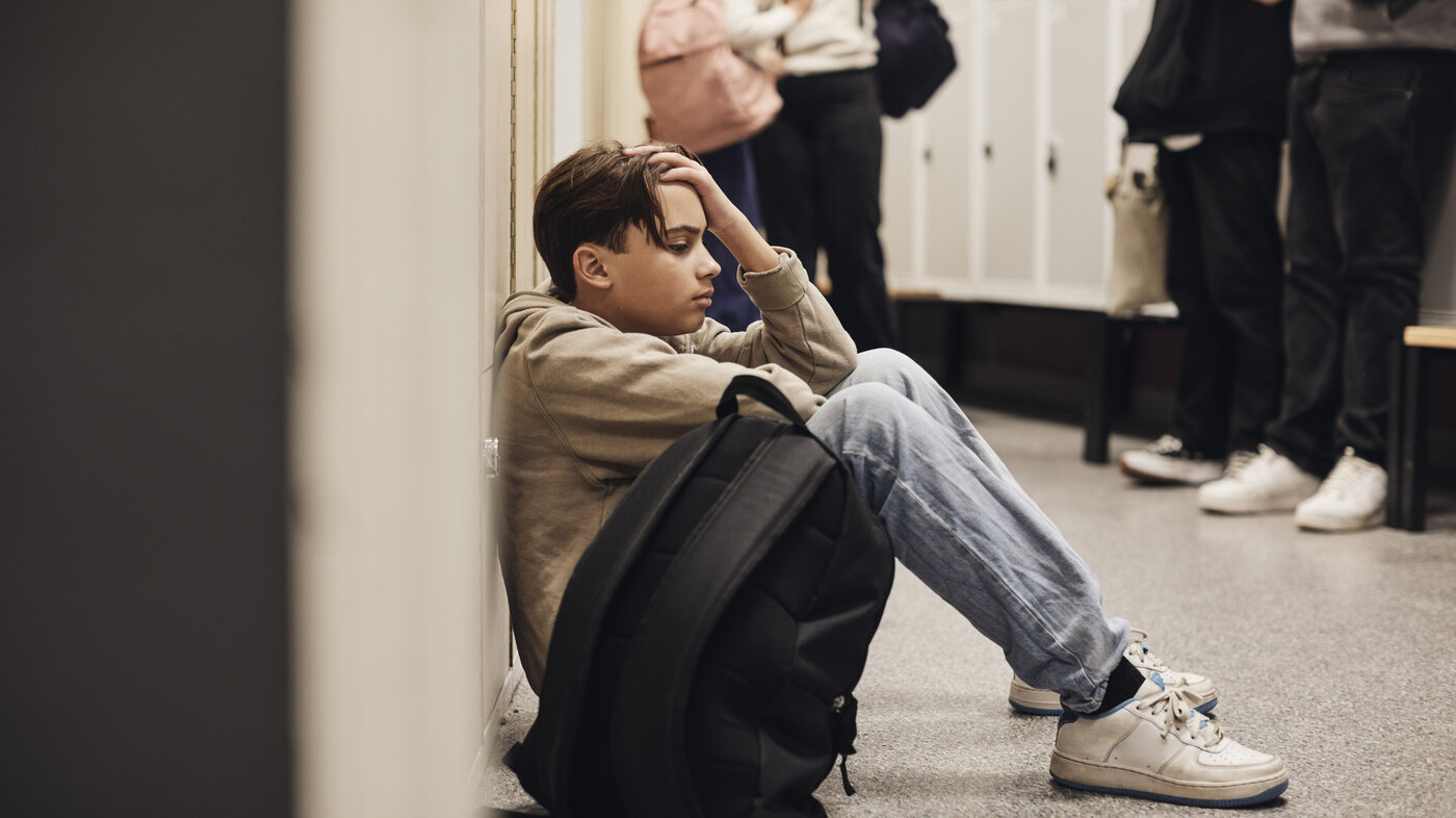 Bildet viser en bedrøvet, ung gutt som sitter på gulvet i en skolekorridor