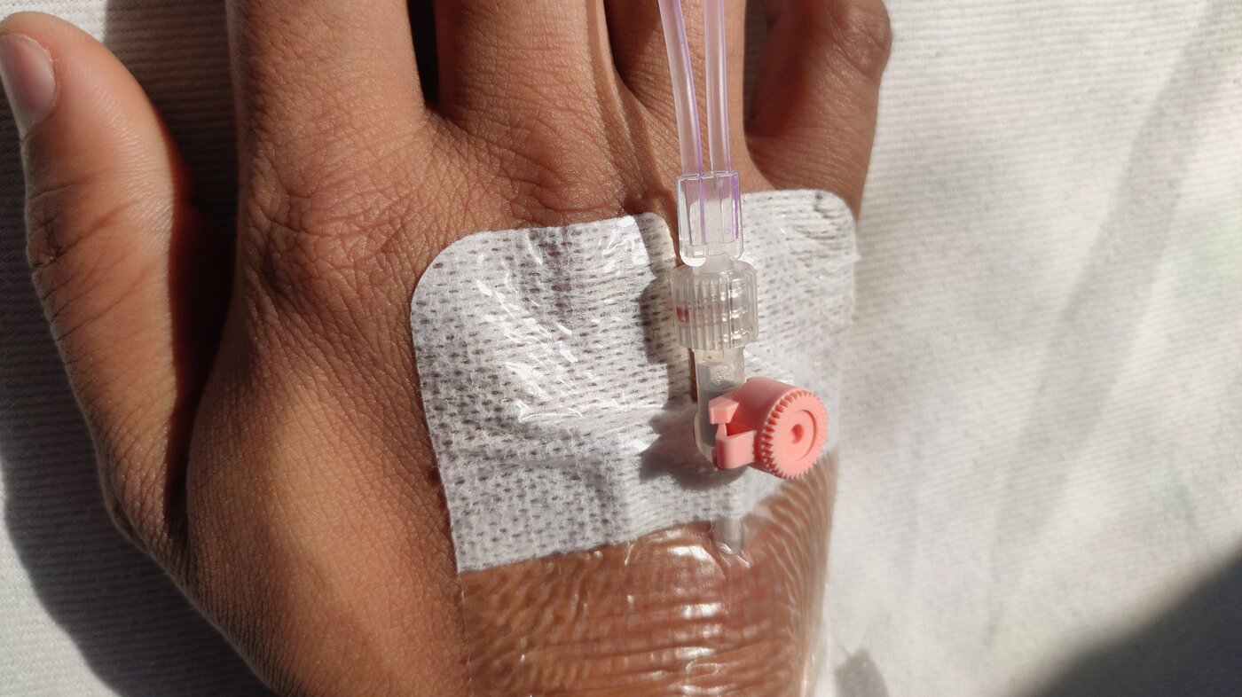 The photo shows a hand with a venous catheter in the vein