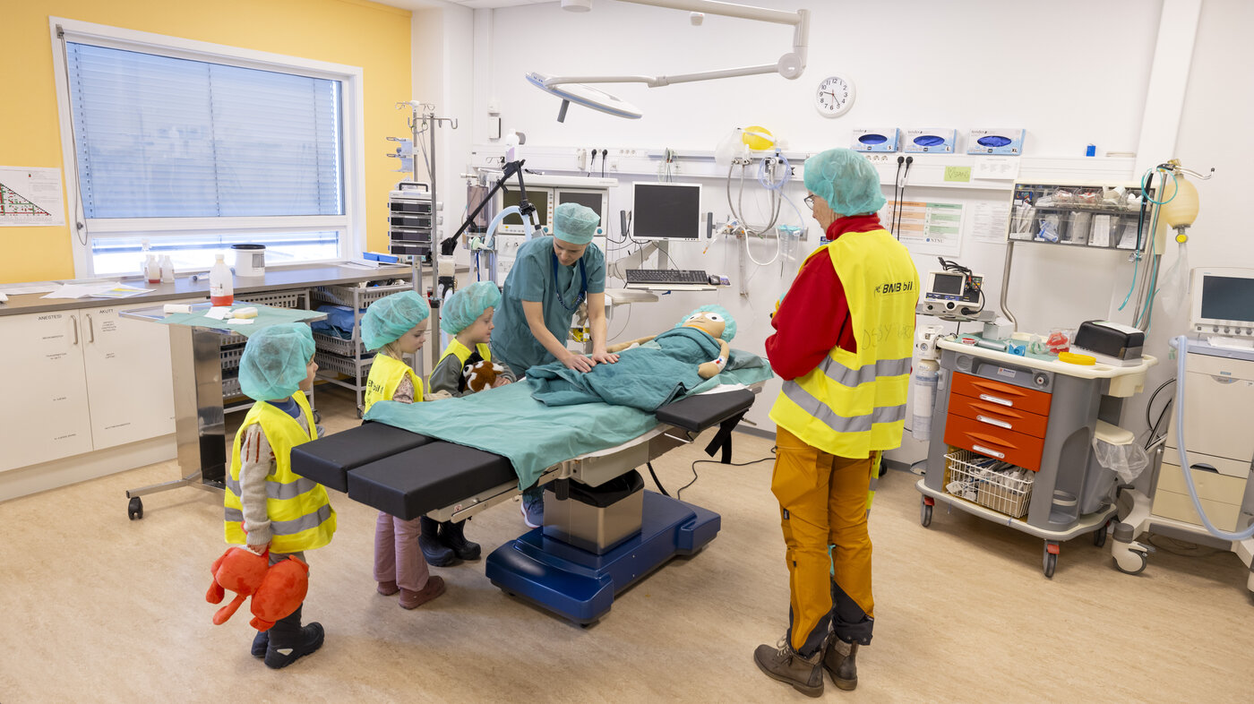 Bildet viser barn sammen med helsepersonell. På båren ligger en tøydukke som blir undersøkt.