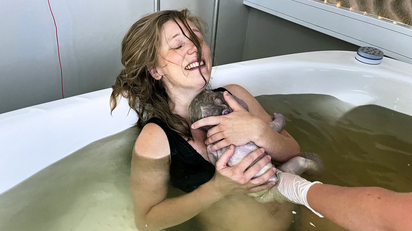 The photo shows a woman who has just given birth in water. She is lying in the pool holding her newborn baby in her arms