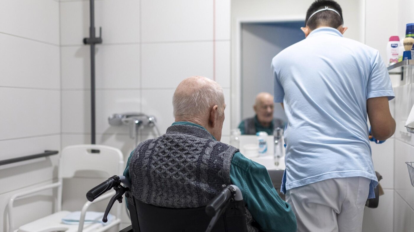 Bildet viser en mannlig sykepleier som steller en eldre pasient på badet