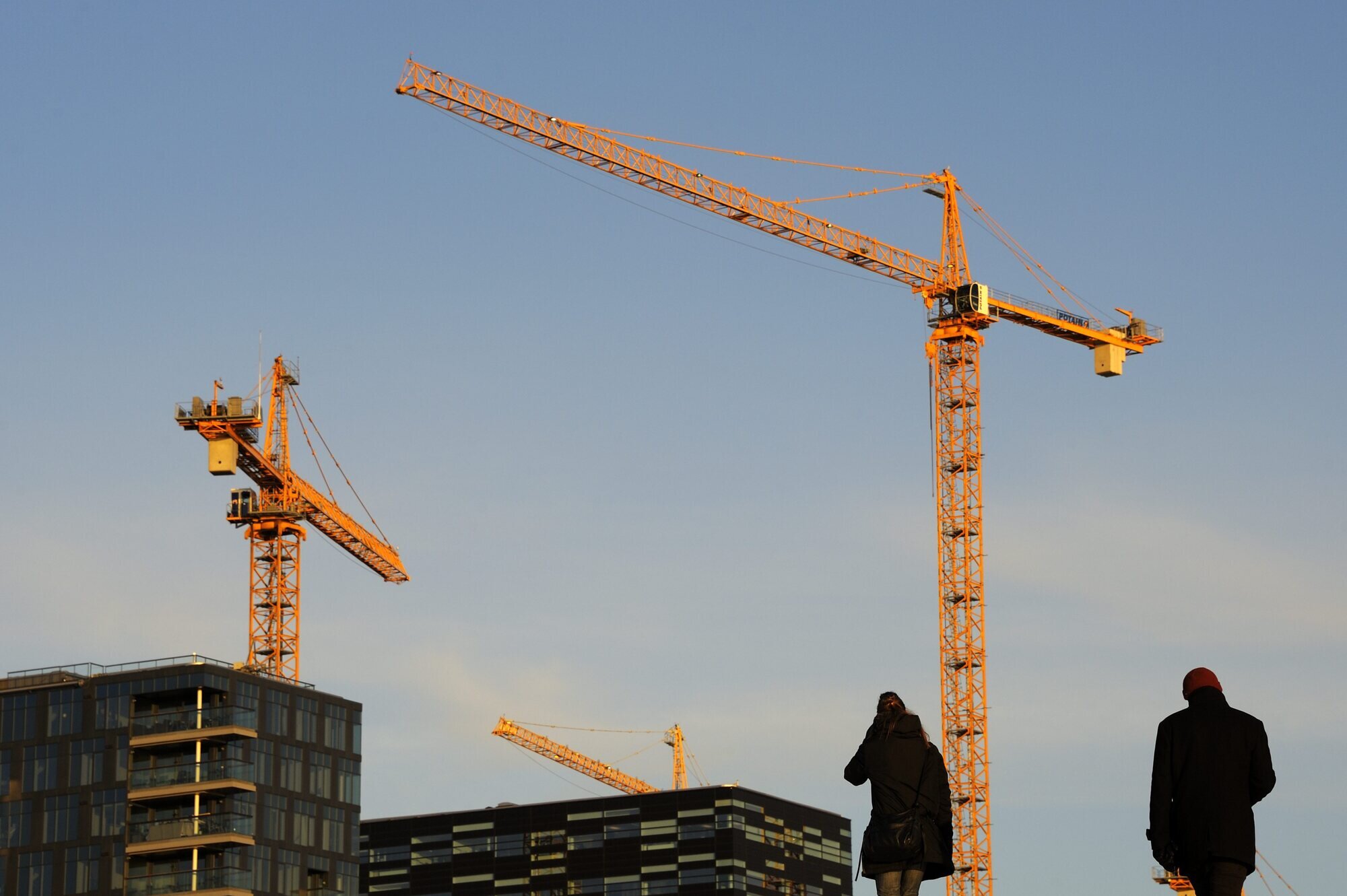 Bildet viser en byggeplass med to mennesker i siluett i forgrunnen Bildet viser en byggeplass med to mennesker i siluett i forgrunnen