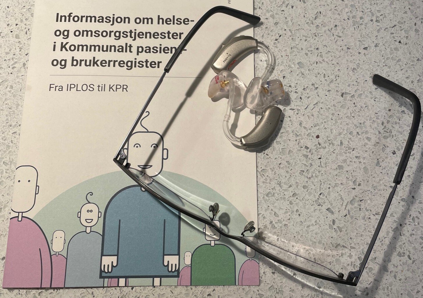 Bildet viser briller, høreapparat og et hefte fra Helsedirektoratet