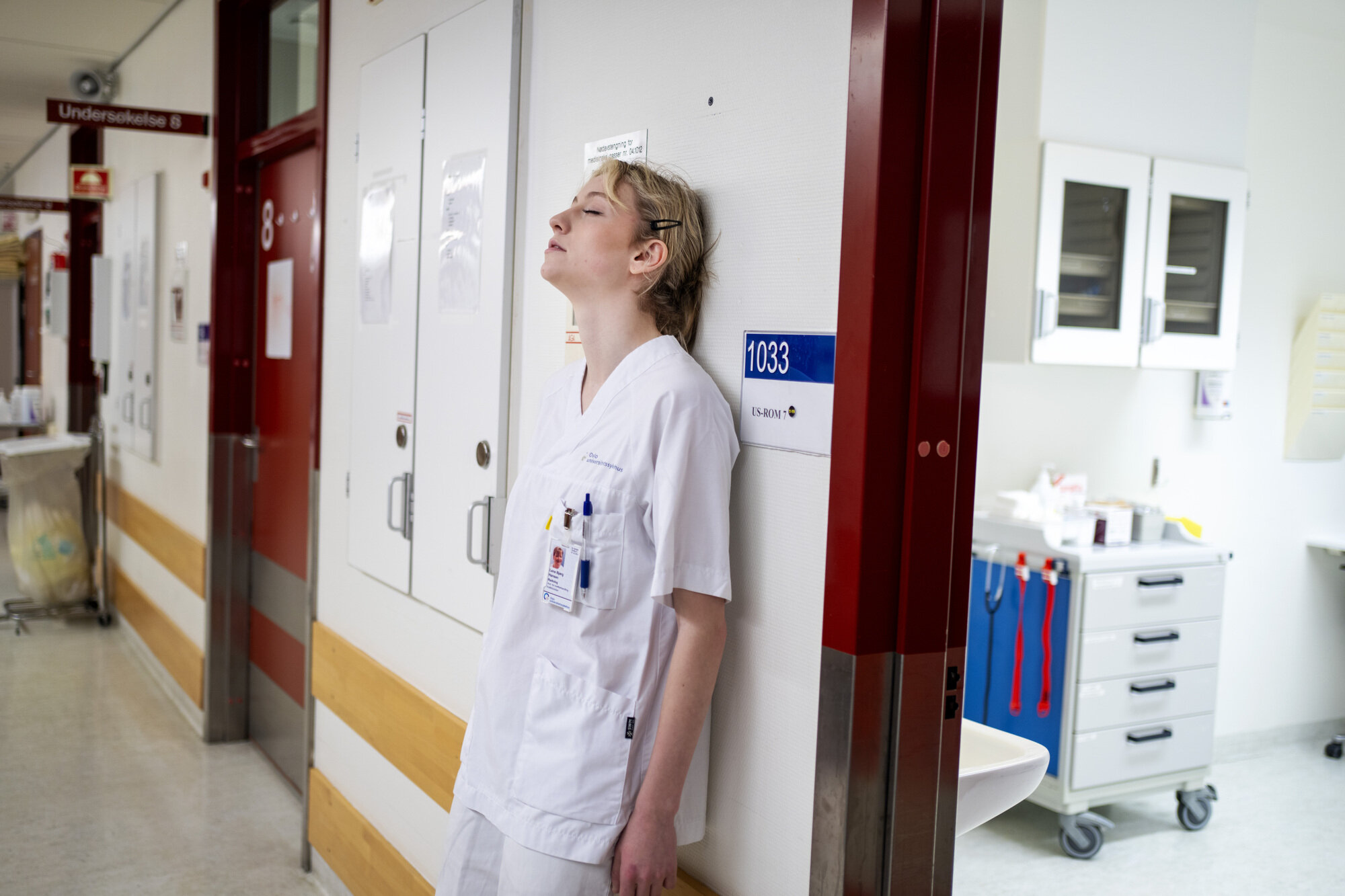 Bildet viser en sliten sykepleier som er lent mot veggen med ryggen.