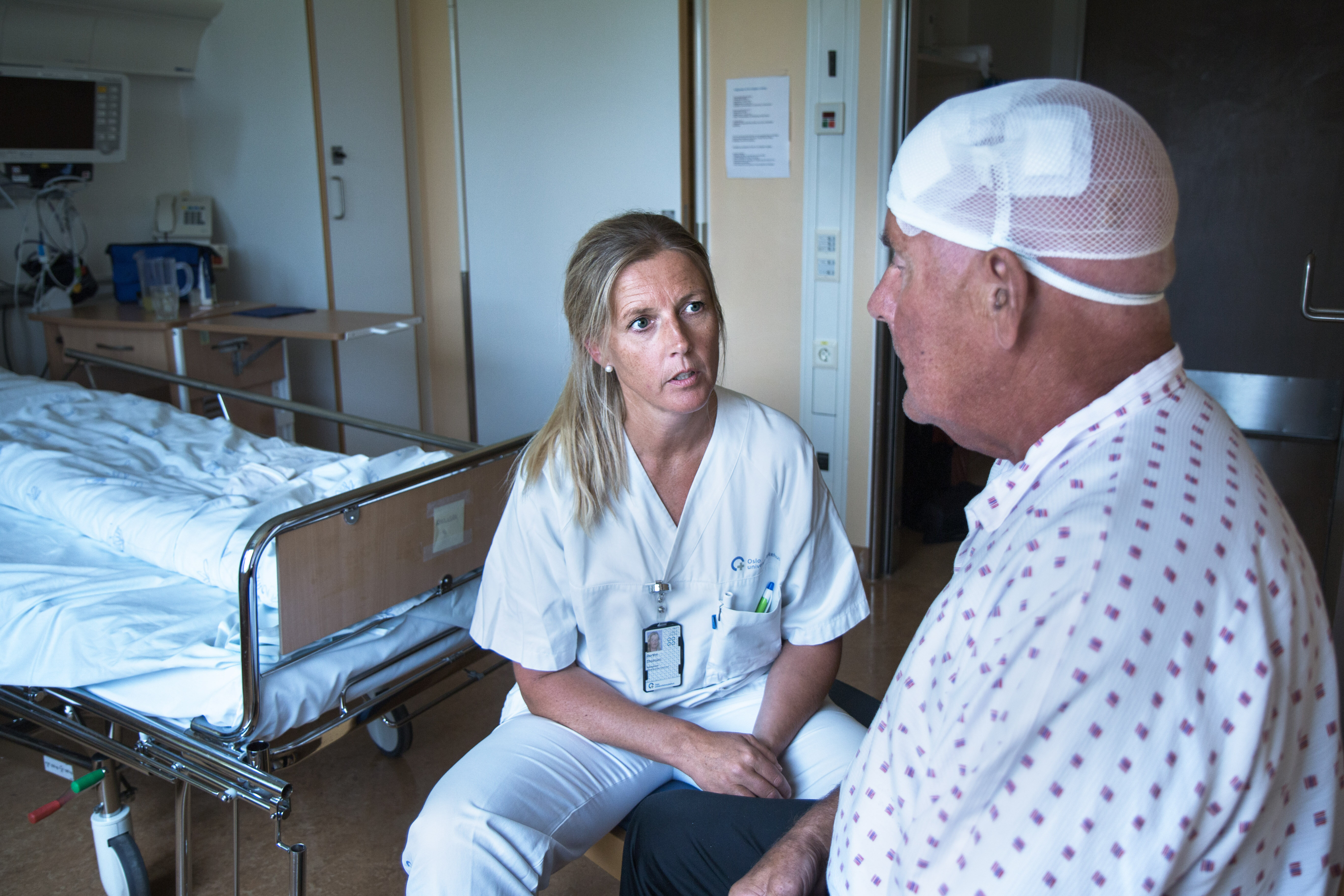 Parkinsonsykepleier Bildet viser en sykepleier som sitter overfor en nyoperert parkinsonpasient. Han har bandasje rundt hodet