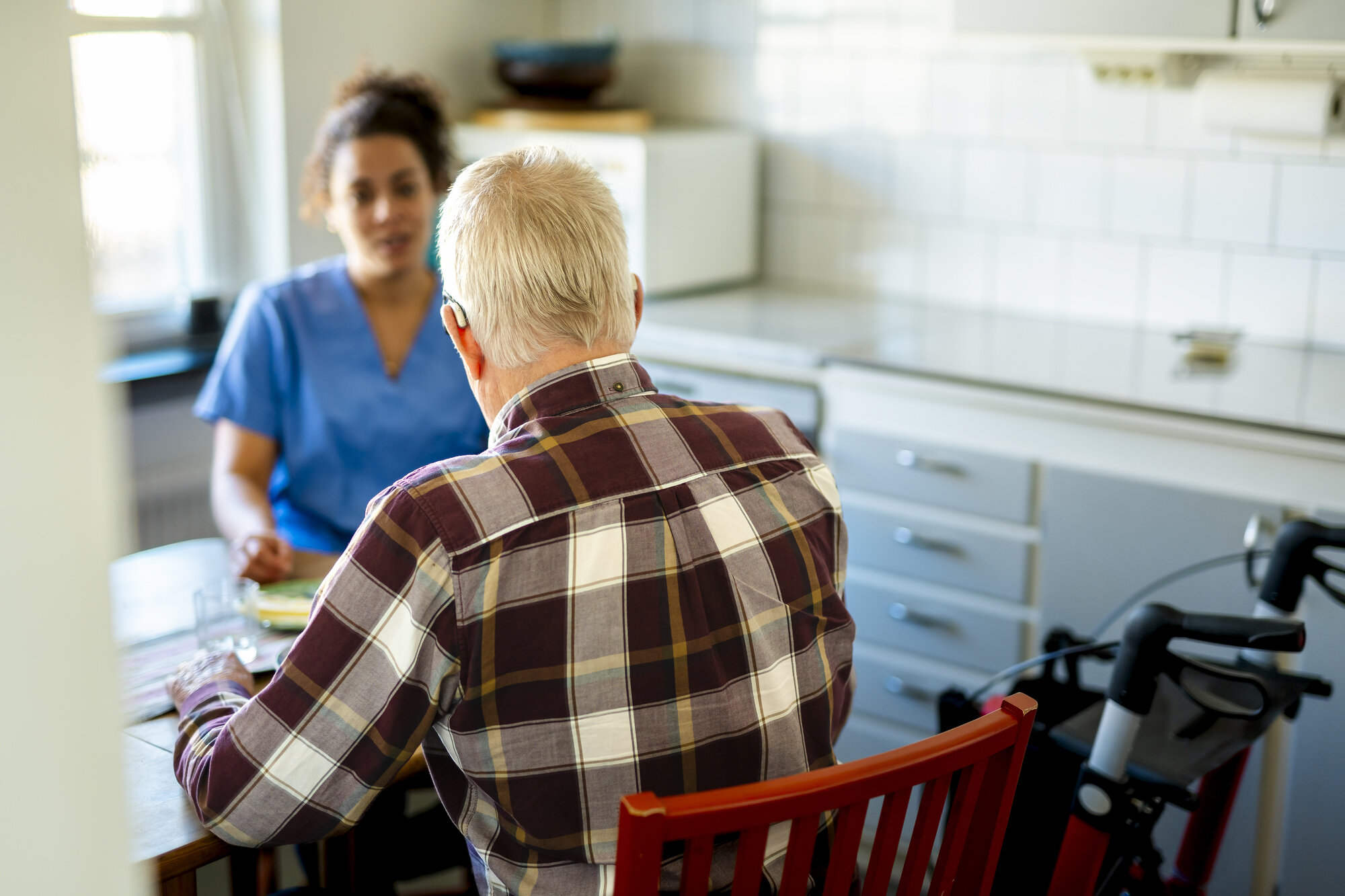 Bildet viser en mann som sitter med ryggen til kamera, vendt mot en pleier.