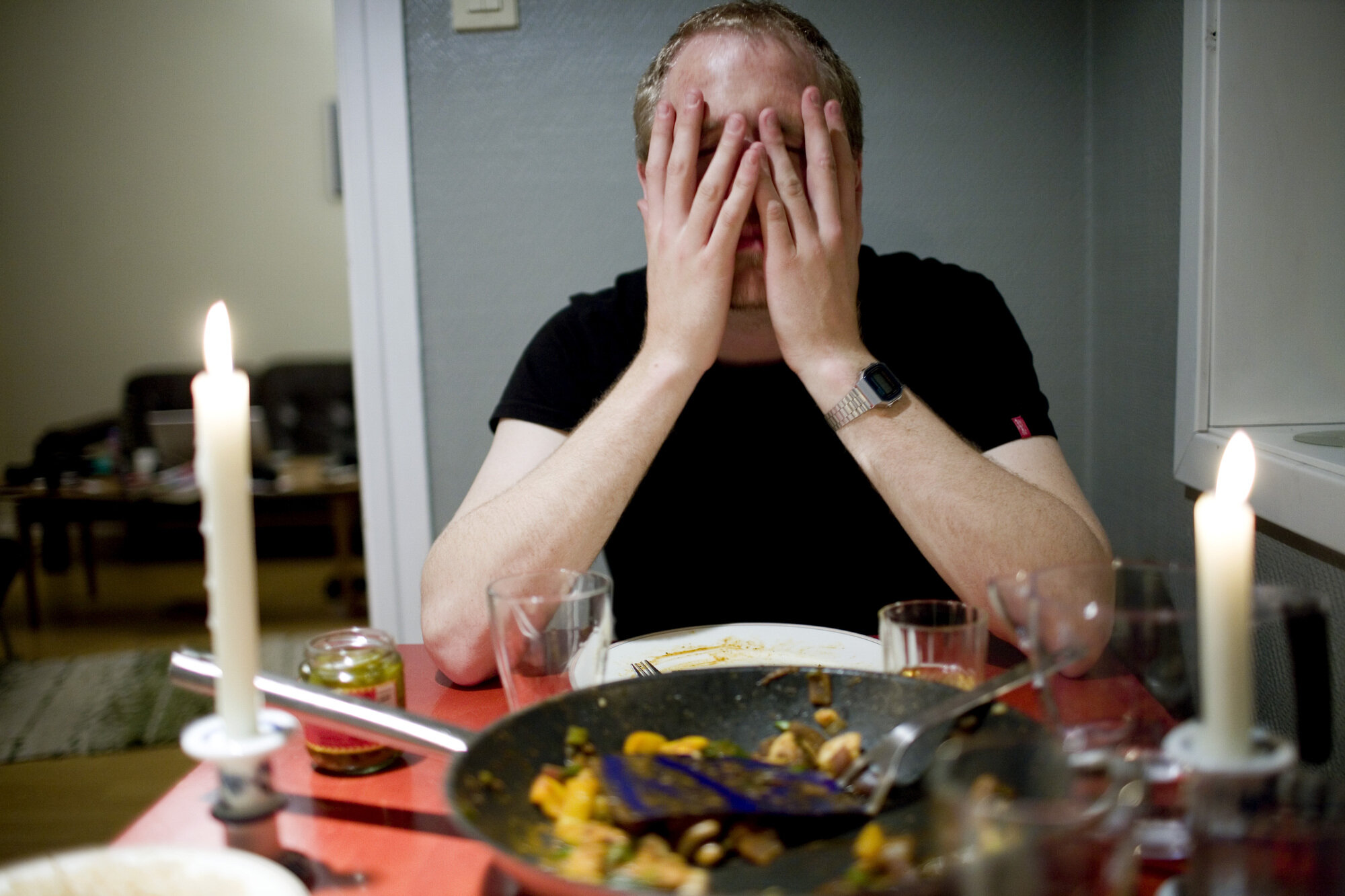 Bildet viser en mann som sitter ved et spisebord og holder seg til ansiktet.