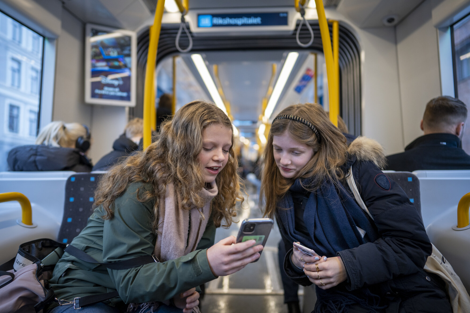 Bildet viser to unge jenter som ser på mobilene sine på trikken.