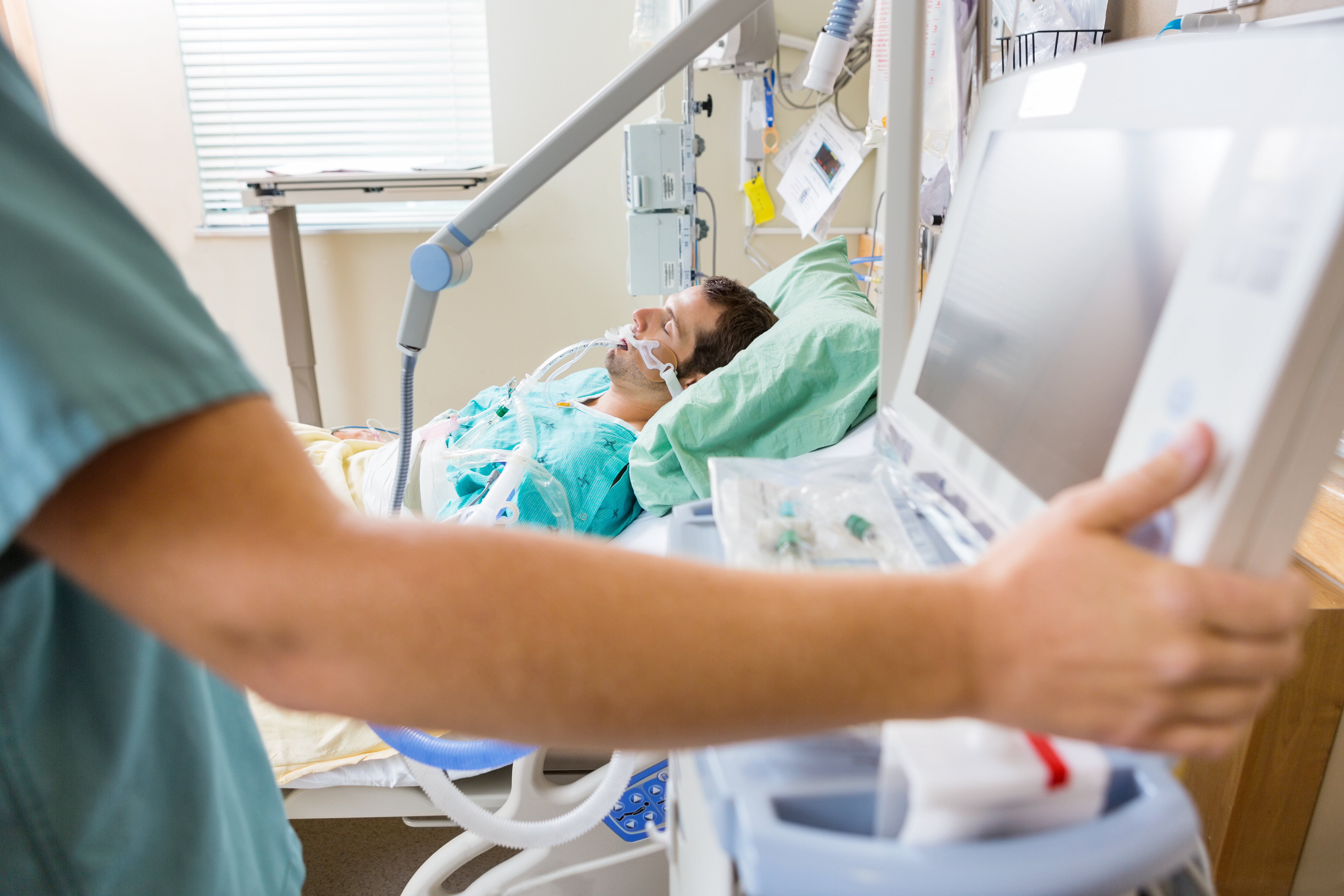 The photo shows nurse pressing monitor's button with male patient lying on bed in hospital