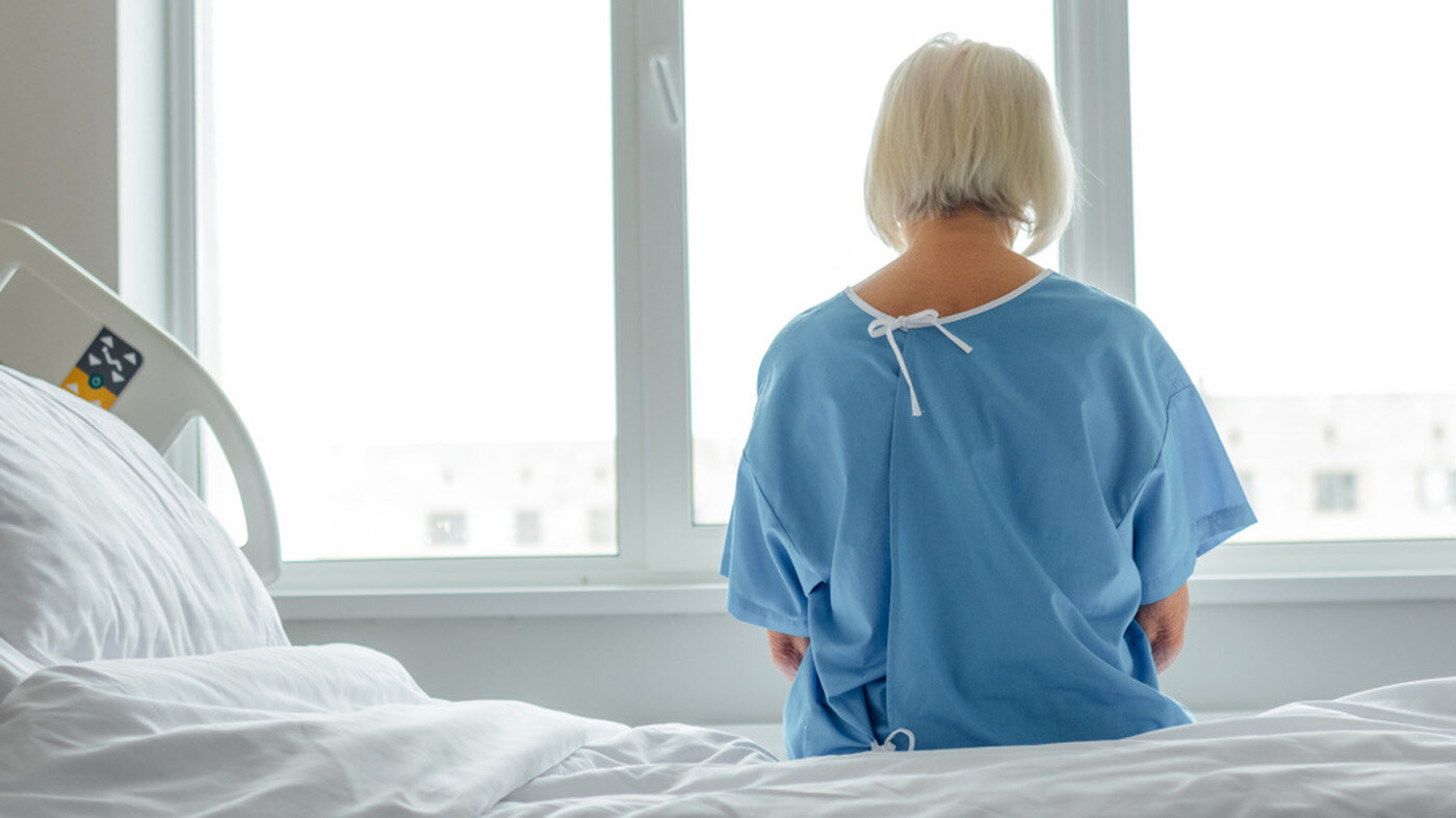 Bildet viser en pasient bakfra. Hun sitter på en sykehusseng og ser framfor seg.