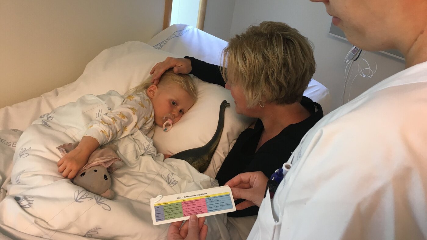 Lite barn i sykehussengen får hjelp av sykepleier til å forklare smerte.