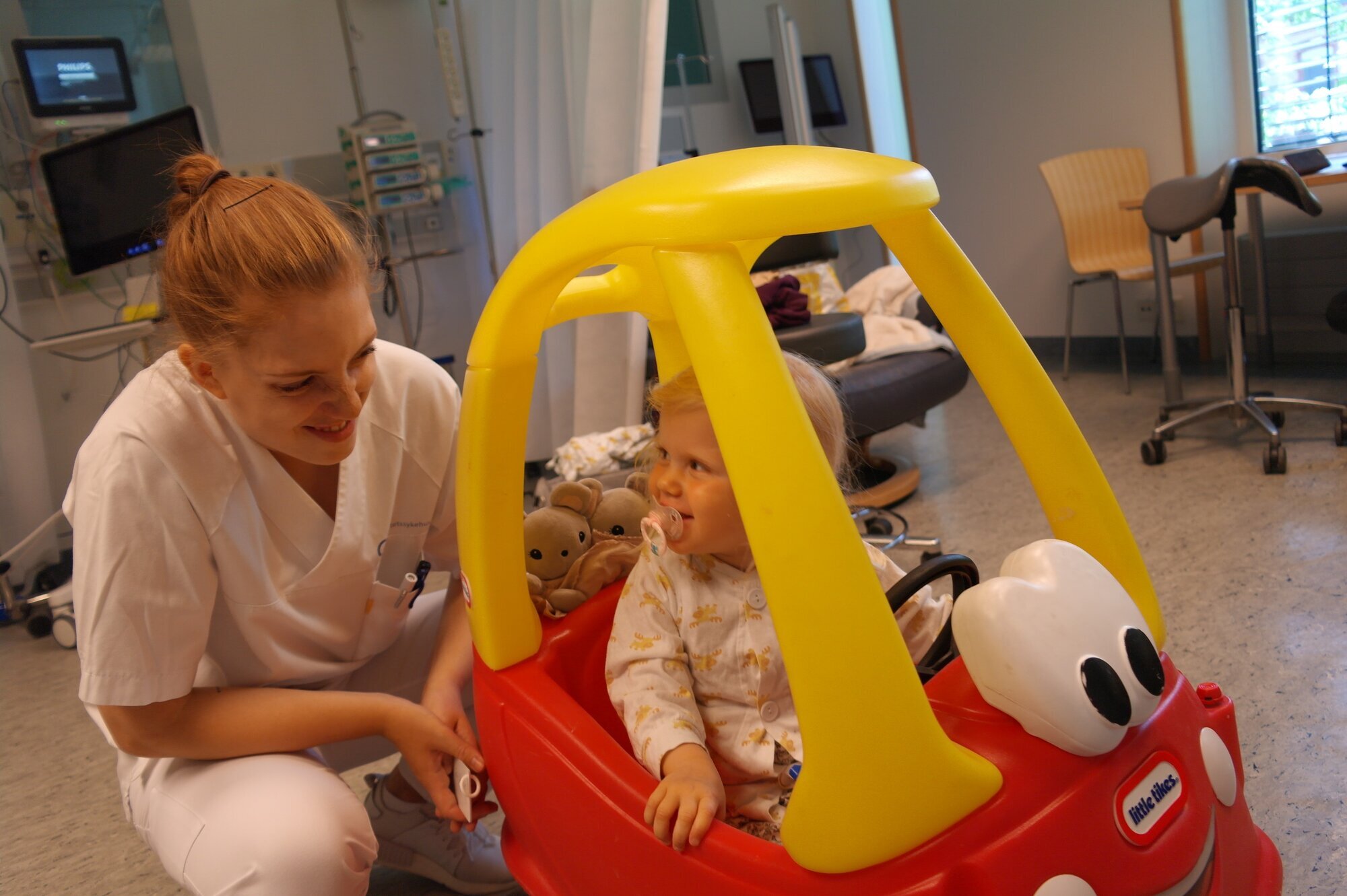 Sykepleier snakker med et lite barn i en lekebil på et sykehus. Sykepleier snakker med et lite barn i en lekebil på et sykehus.