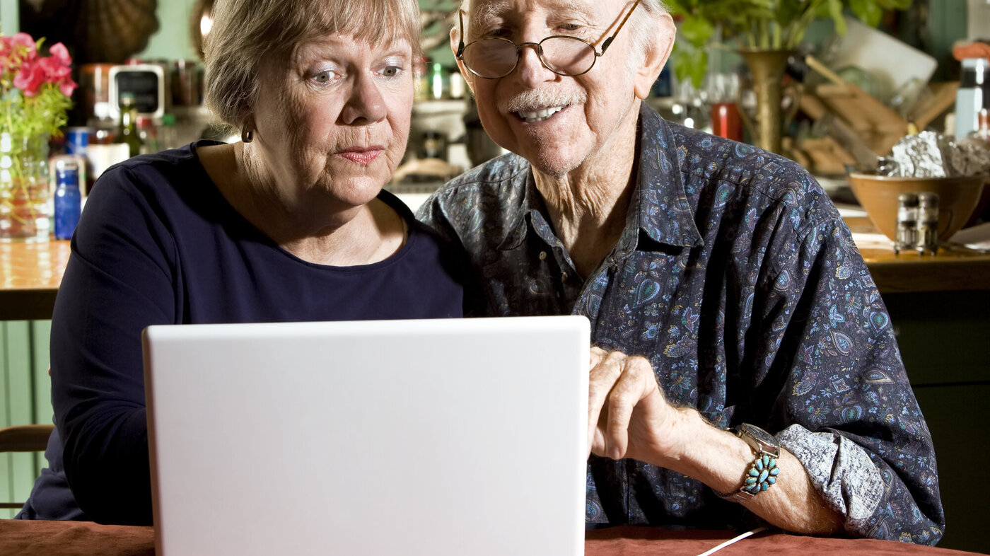 Bildet viser to eldre personer som sitter foran en laptop