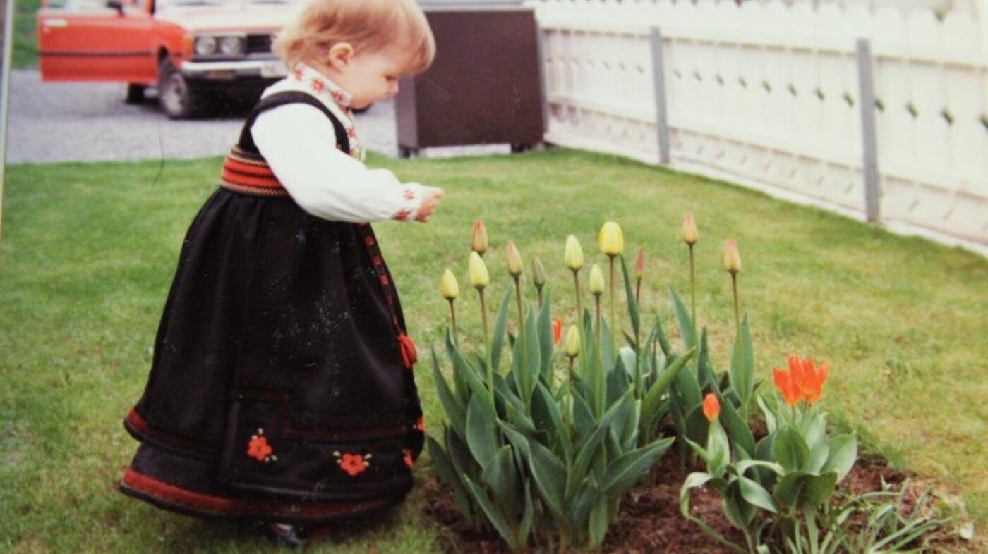 Bildet viser Lillian Elise Esborg Bergane som liten i bunad og som ser på tulipaner i knopp.