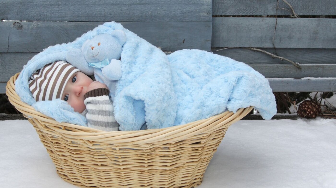Bilde av en liten baby som ligger i en kurv med blått teppe.