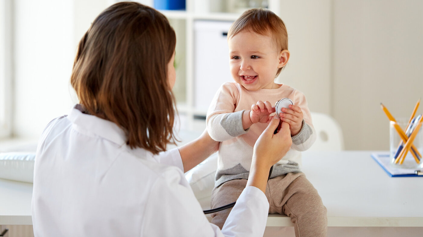 En baby undersøkes av en helsearbeider. En blid baby sitter på et bord og blir undersøkt av en helsearbeider.