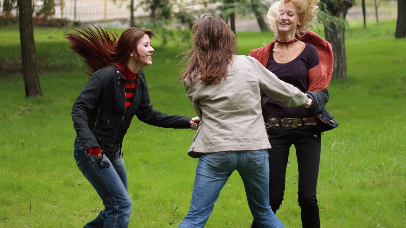 Tre kvinner danser i ring ute i en park