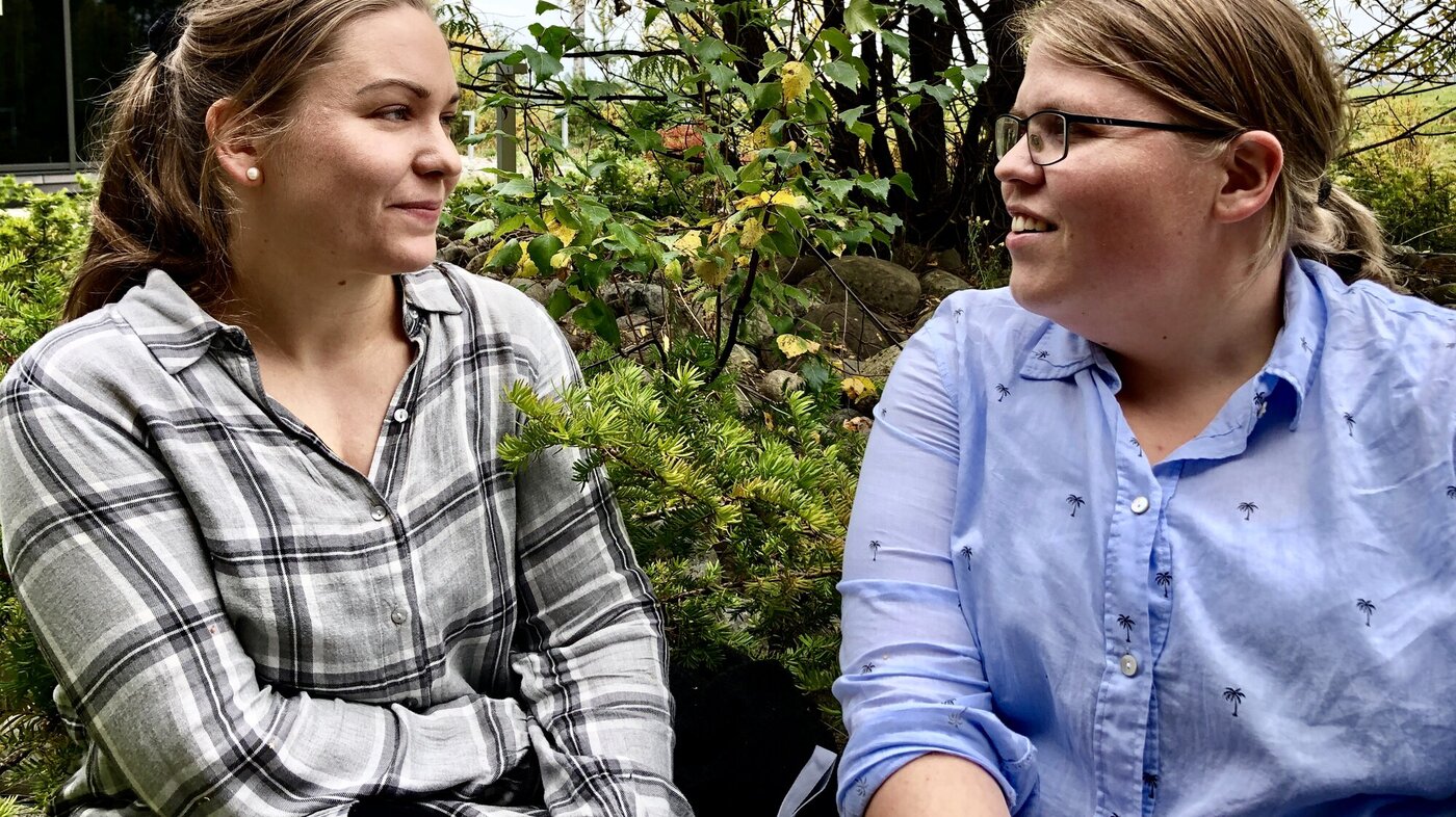 To unge damer se mot hverandre, sitter ute i høstlig landskap