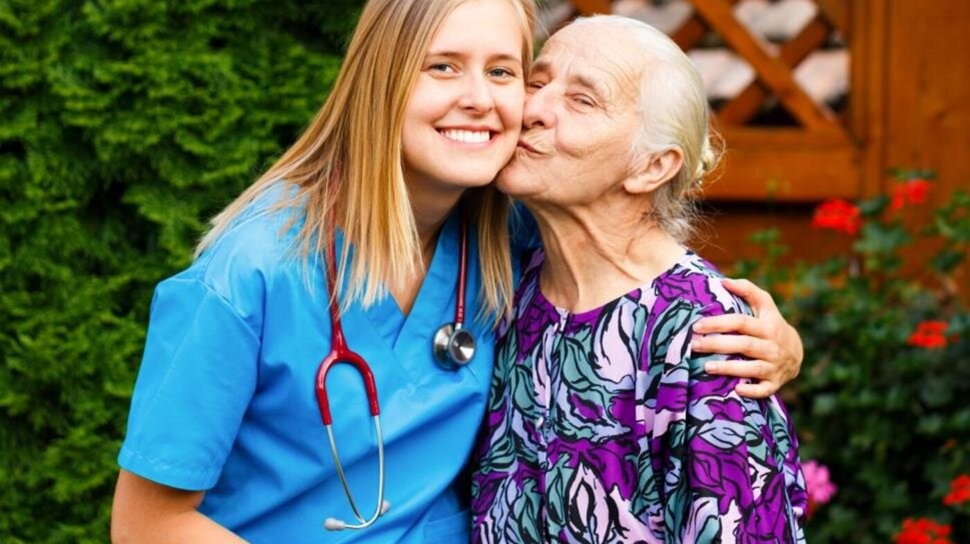 Bildet viser en ung lege som kysses på kinnet av en eldre pasient.