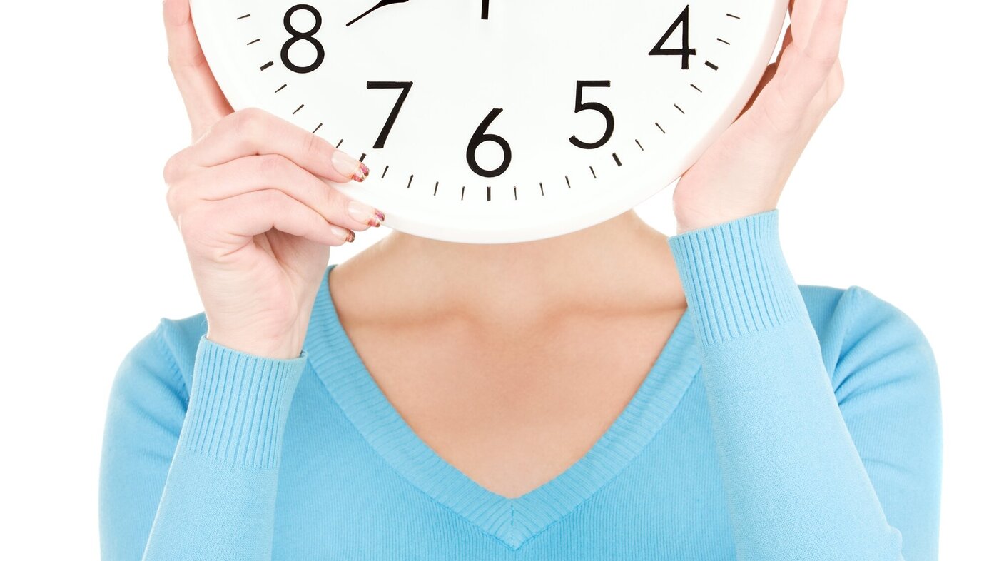 Bildet viser overkroppen til en kvinne som holder en klokke foran ansiktet.