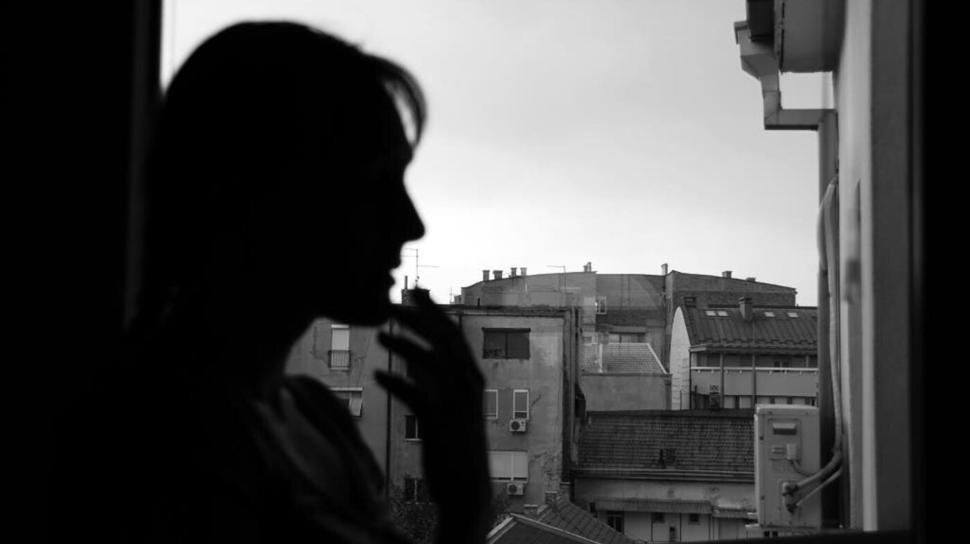 Bildet viser silhuetten av en kvinne ved et vindu med urban utsikt.