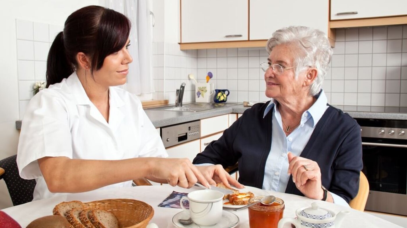 Sykepleier spiser et måltid med en eldre dame