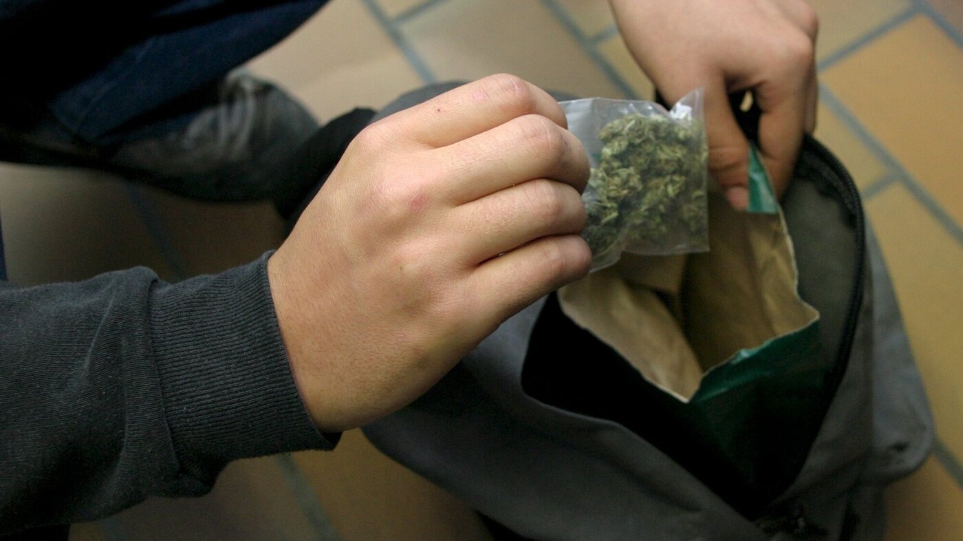 Bildet viser en ungdom som tar opp en pose marihuana av skolesekken