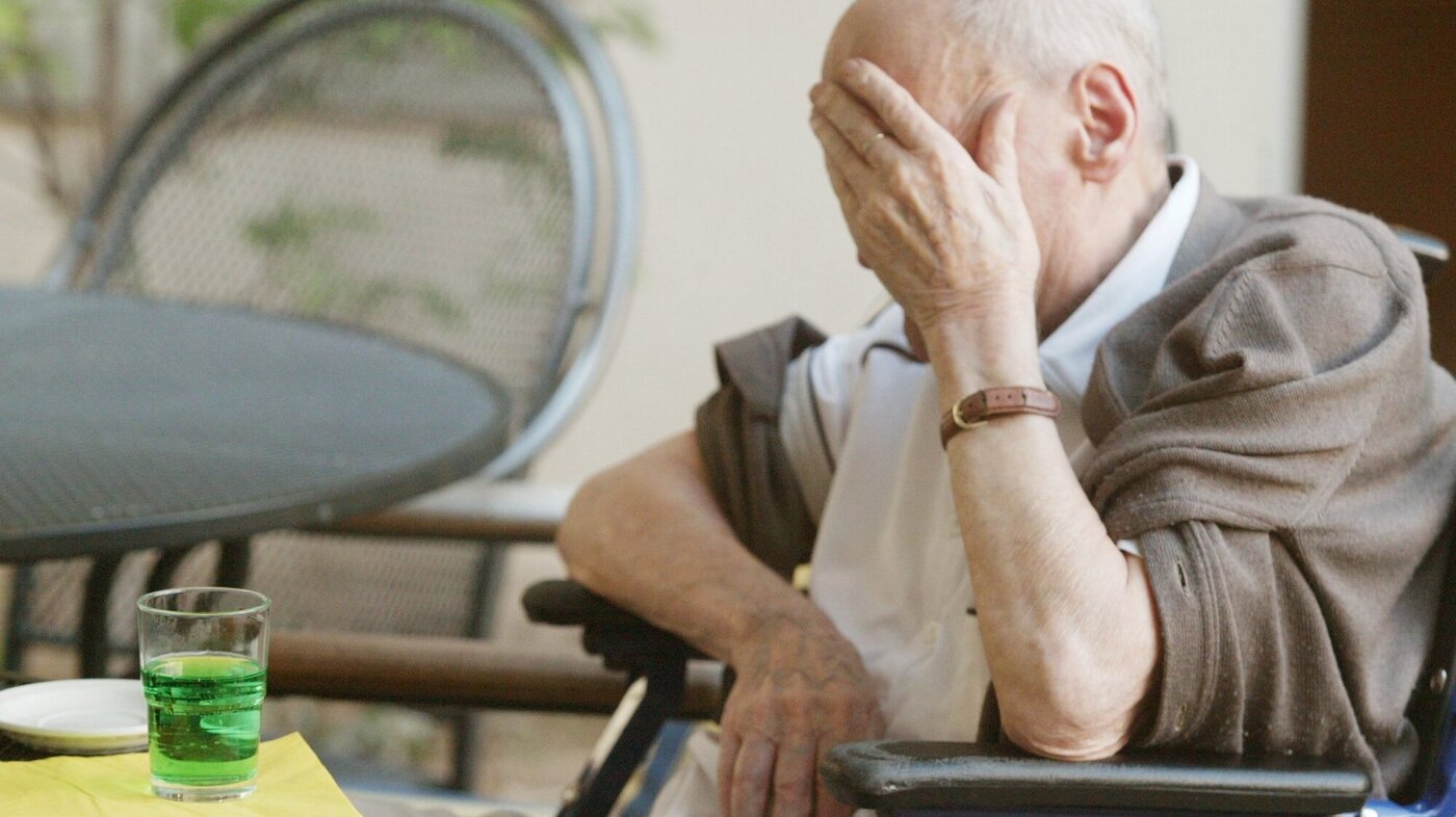 Bildet viser en eldre mann som holder seg til ansiktet i fortvilelse.