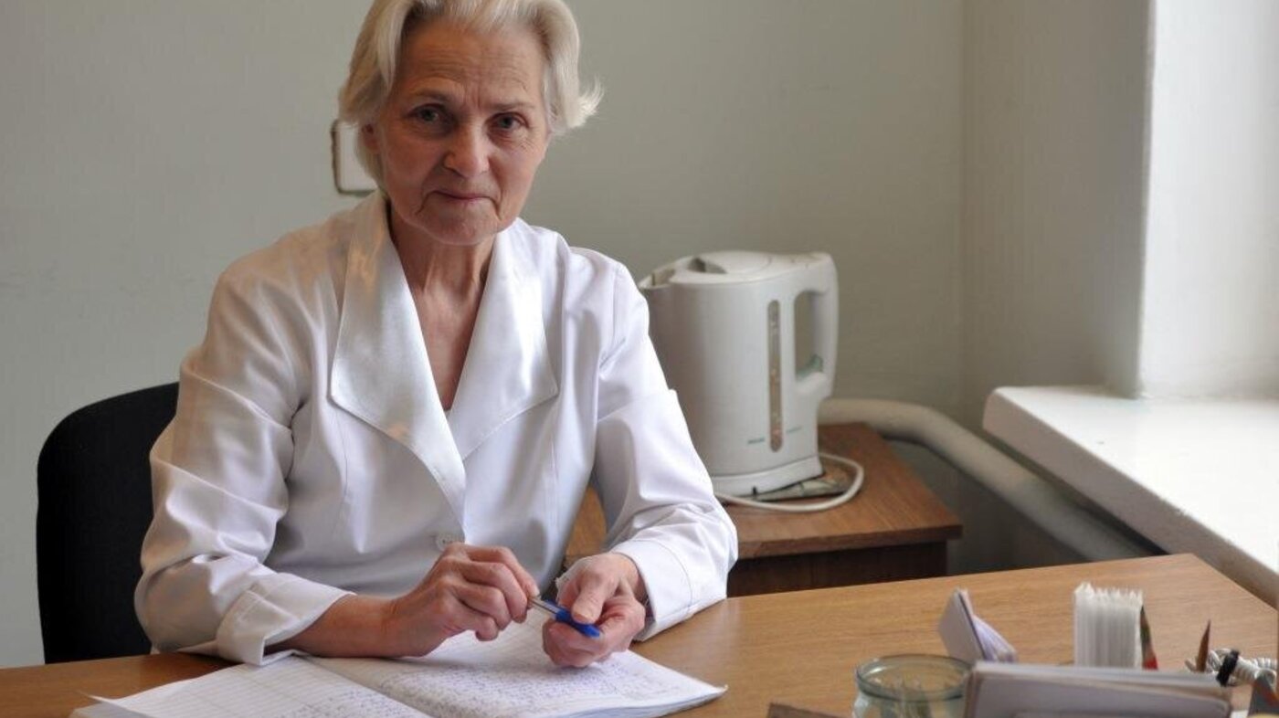 Helseminister Høie ønsker å la sykepleiere og annet helsepersonell beholde autorisasjonen til fylte 80 år. Bildet viser en eldre, kvinnelig helsearbeider bak et skrivebord.