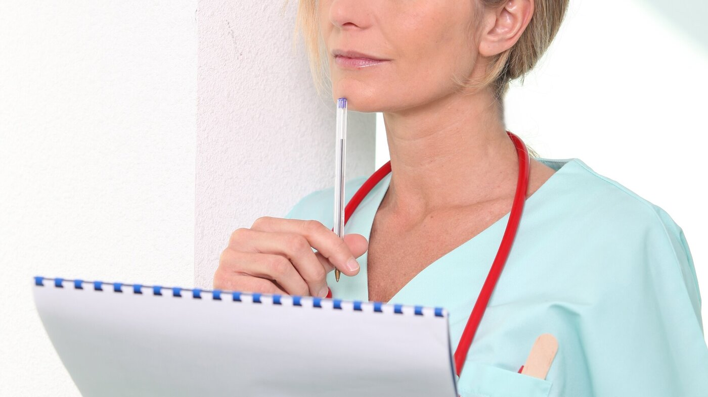 En kvinnelig sykepleier står og tenker med en penn og skriveblokk