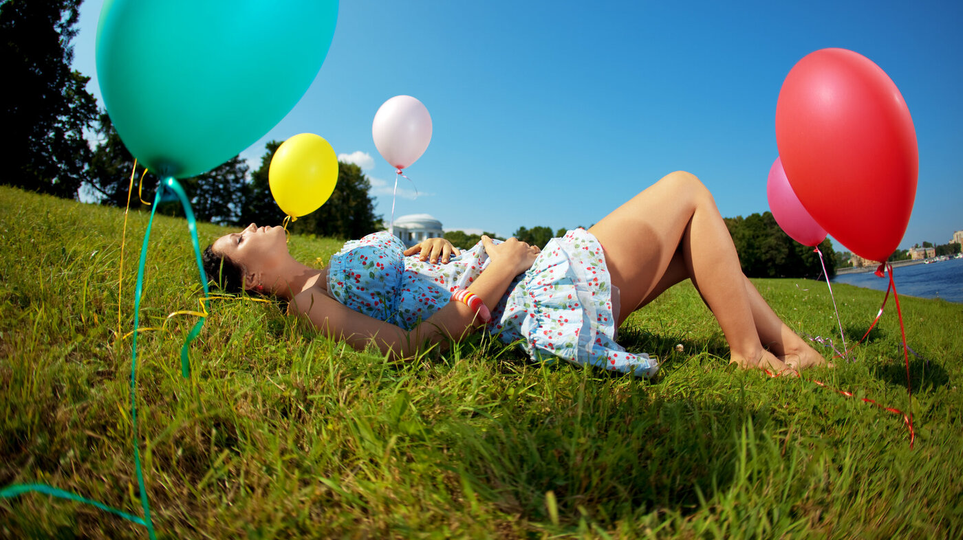 Bildet viser en gravid kvinne liggende i en eng med ballonger rundt omkring.