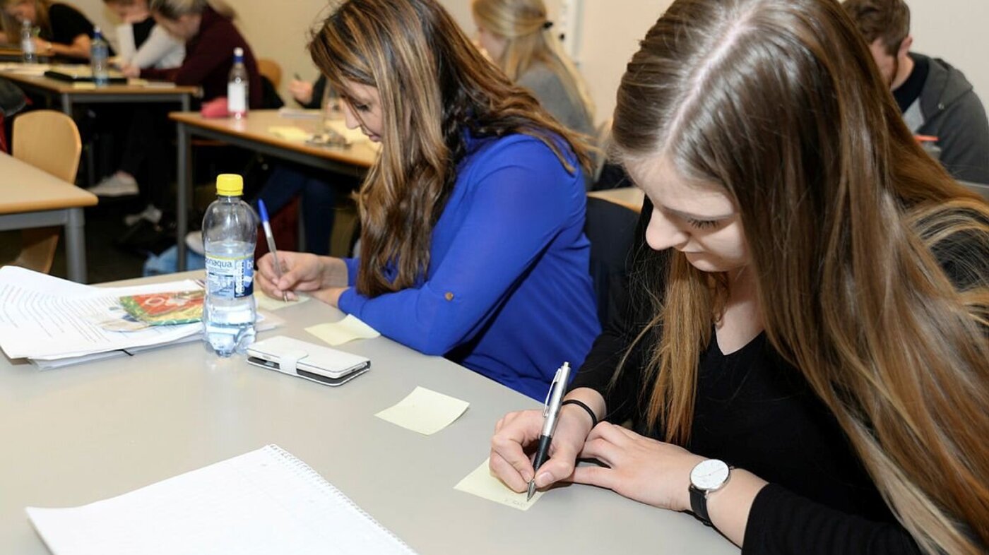 Bildet viser to kvinnelige studenter som sitter ved pultene på Universitetet i Agder