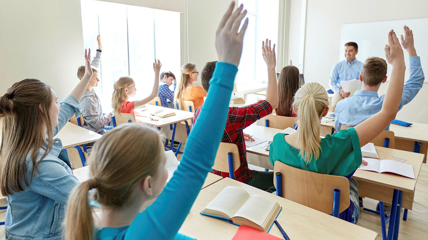 Bildet viser elever i et klasserom som rekker opp hånden.