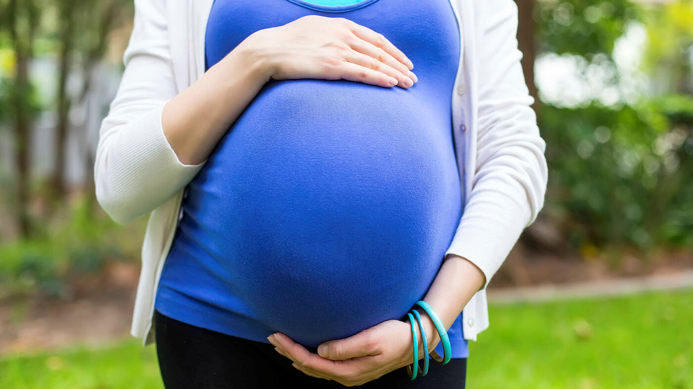 Bildet viser en gravid kvinne med blå topp som holder rundt magen sin