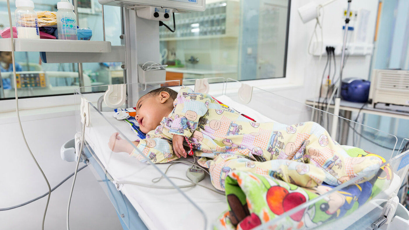 Bildet viser en baby med hjertefeil som ligger i kuvøse på sykehus
