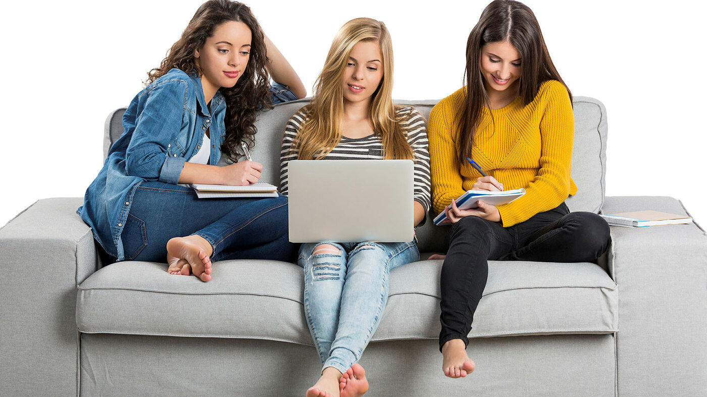 Bildet viser tre unge kvinner som sitter i en sofa med PC og kladdeblokker.