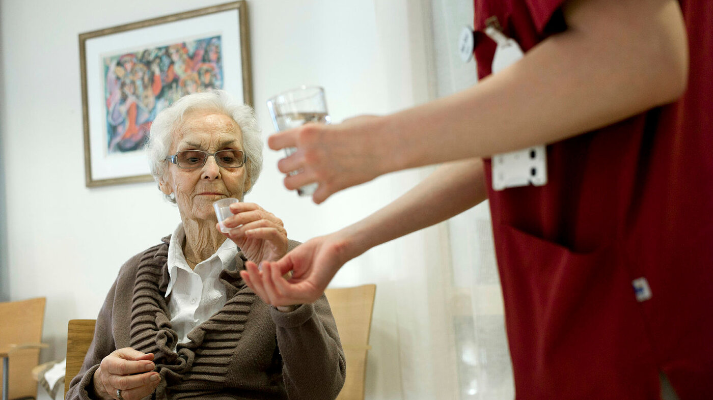 Bildet viser en eldre kvinne som får utdelt medisiner