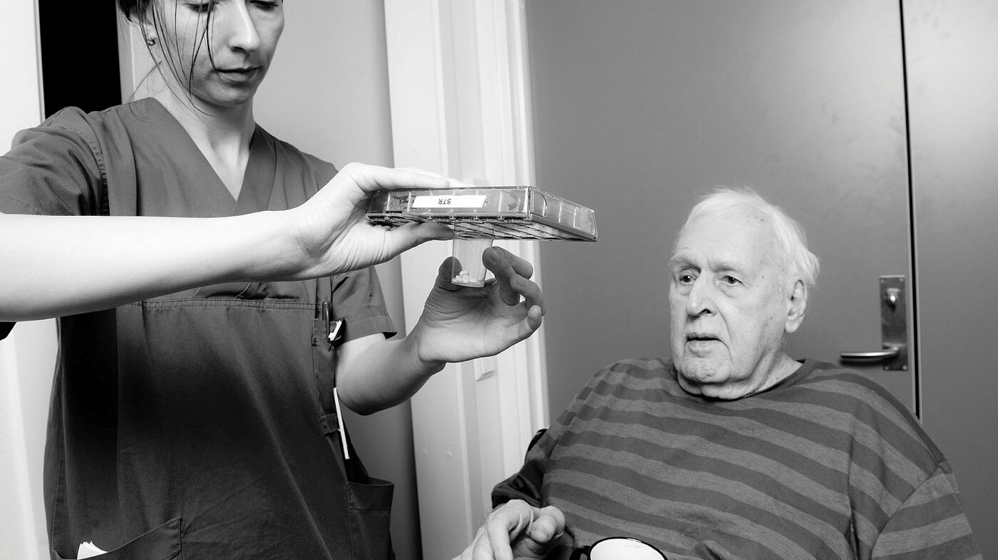 Bildet viser en sykepleier som gir medisiner til en eldre pasient