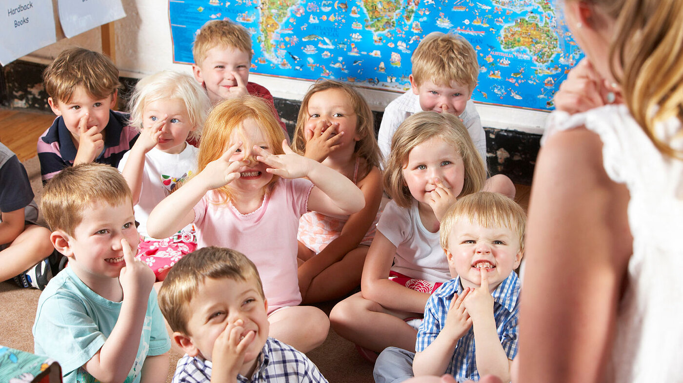 Bildet viser barn i en barnehage som ler sammen med en førskolelærer.