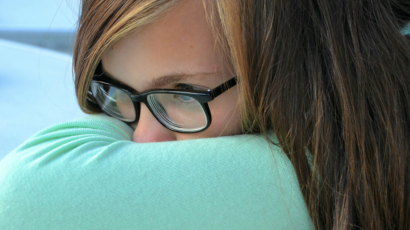 Bildet viser en ung jente som gjemmer ansiktet sitt i en pute