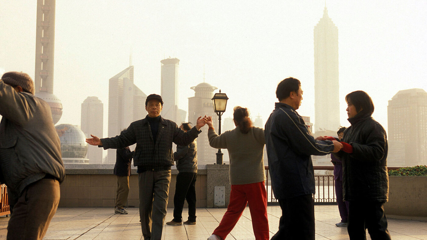 Bildet viser en gruppe eldre mennesker i Shanghai som gjør en form for morgengymnastikk med byen i bakgrunnen.