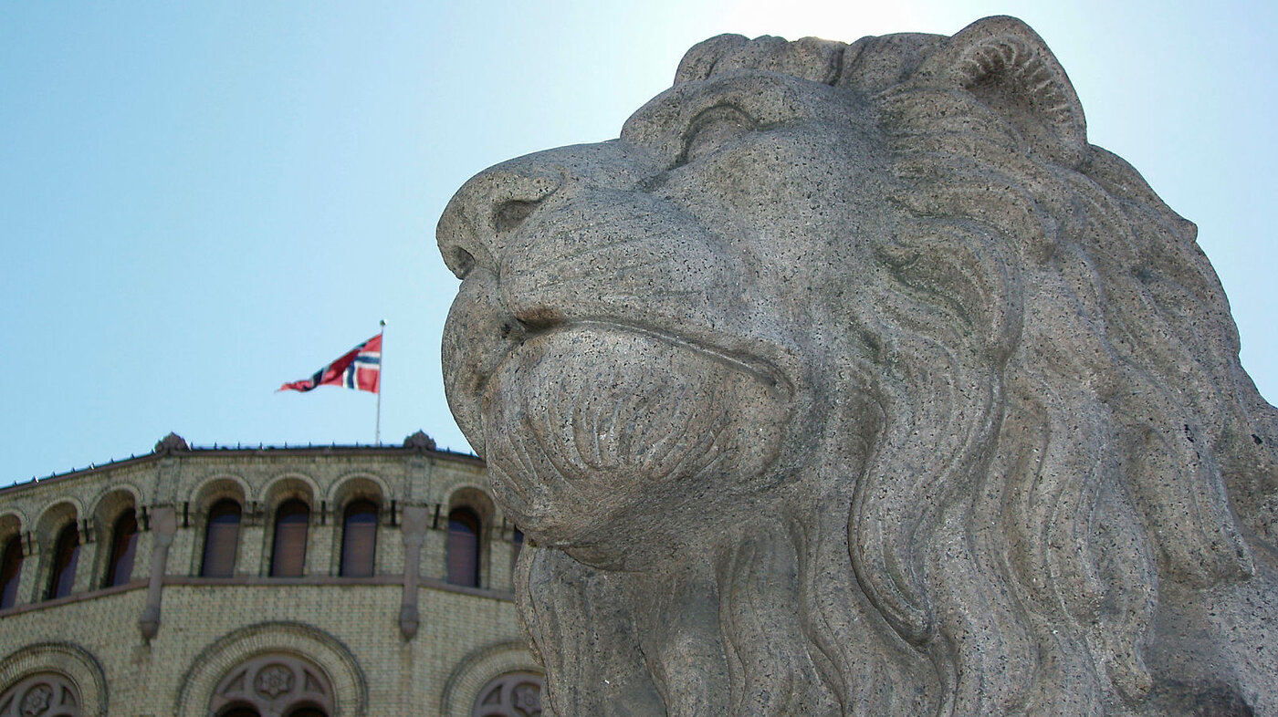 Bildet viser Stortinget og den ene løvestatuen utenfor.
