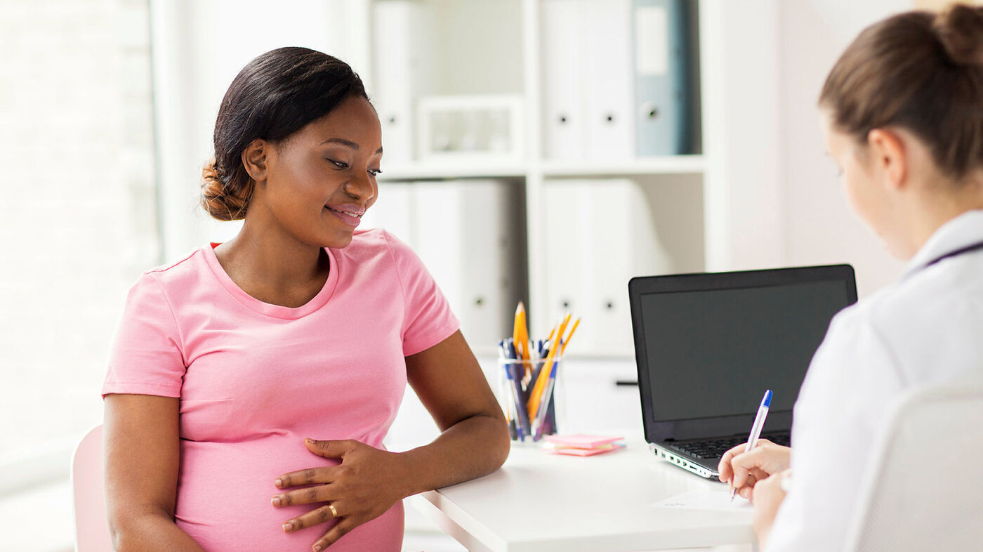 Bildet viser en helsearbeider som sitter med ryggen til og en kvinne som er gravid og på konsultasjon