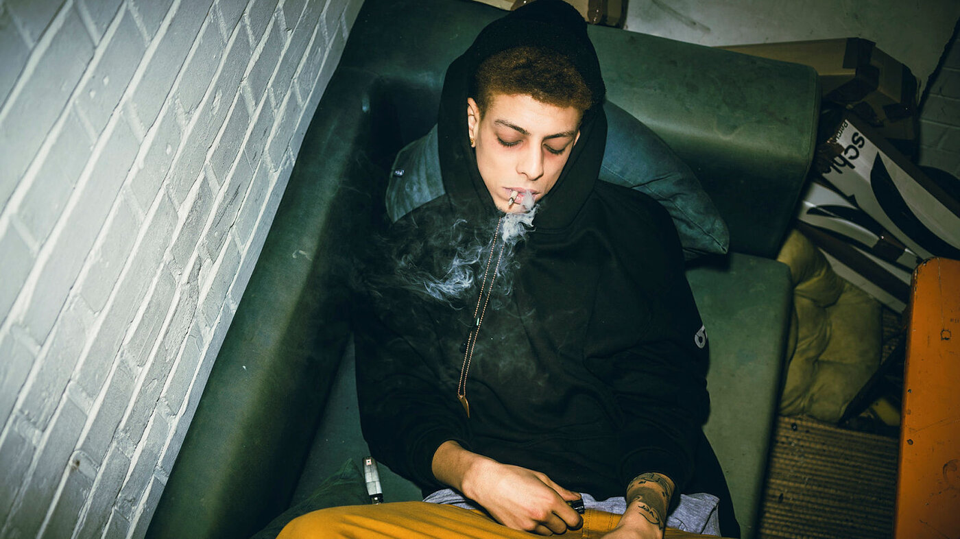 Bildet viser en ung mann som ligger på en sofa og røyker en joint