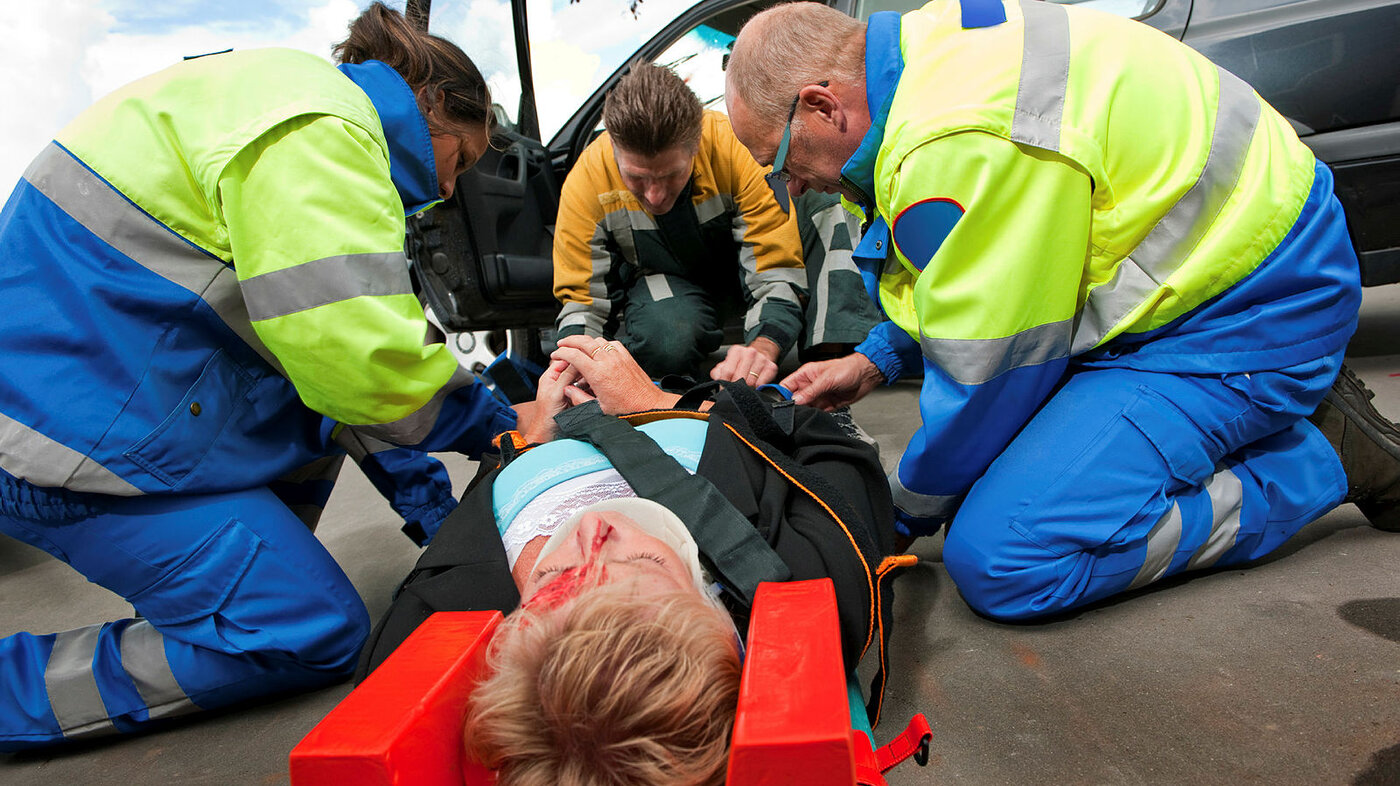 Bildet viser tre ambulansepersonell som gir førstehjelp til en bevisstløs person som har krasjet med bilen.